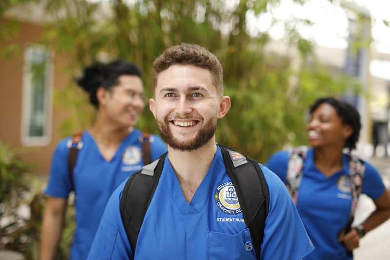 White male nursing student smiling. Two students walk behind him in the background. 